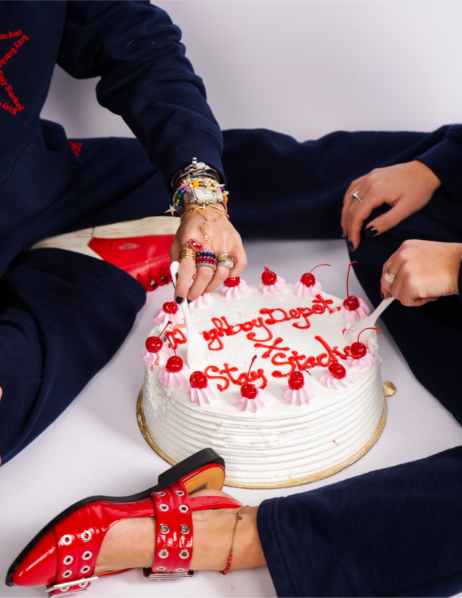 Two individuals are cutting a cake with icing that says "Doughboy Depot X Stay Stacked".